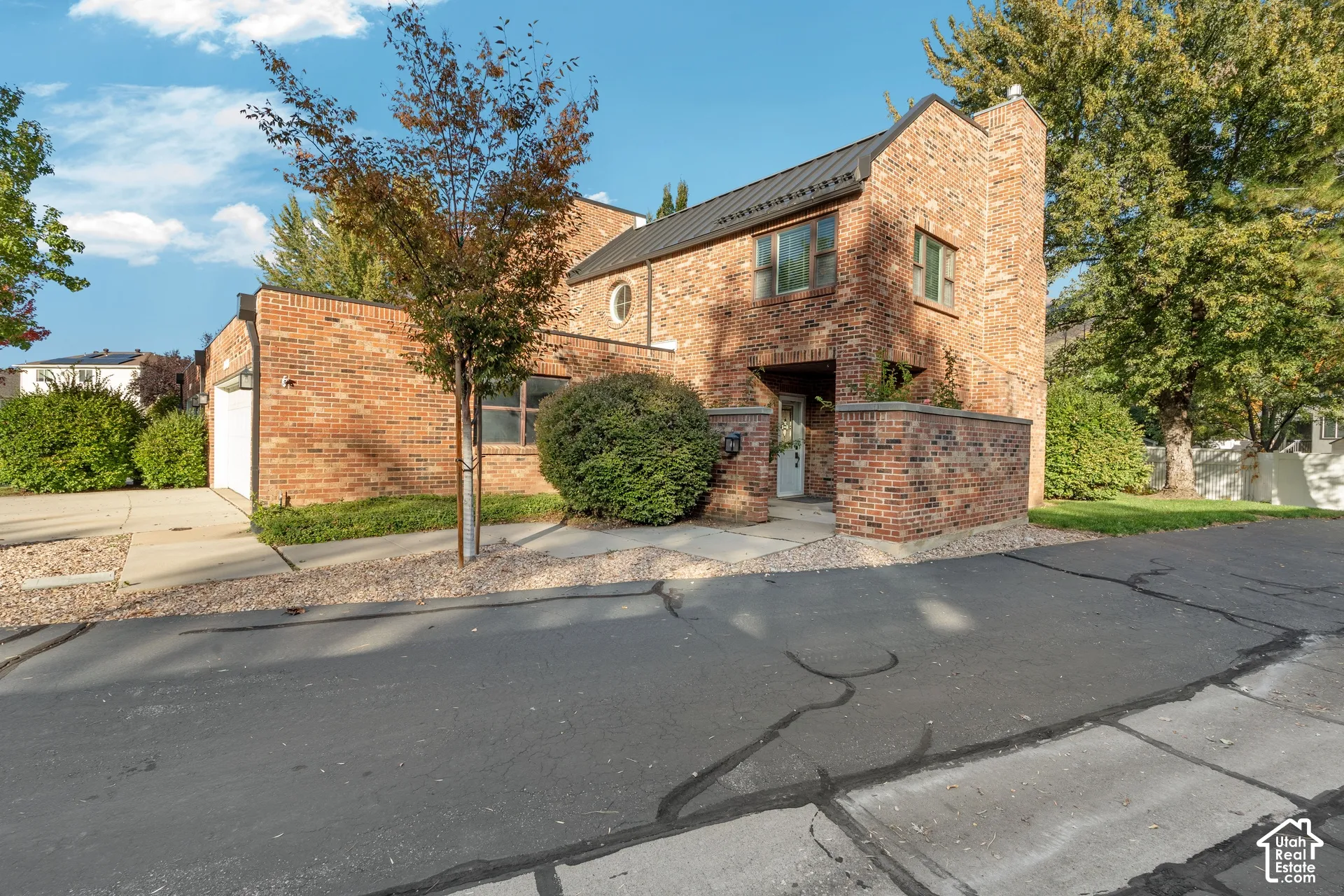 Multi-level brick exterior featuring a metal roof, circular accent window, attached garage, and a gated masonry courtyard entry