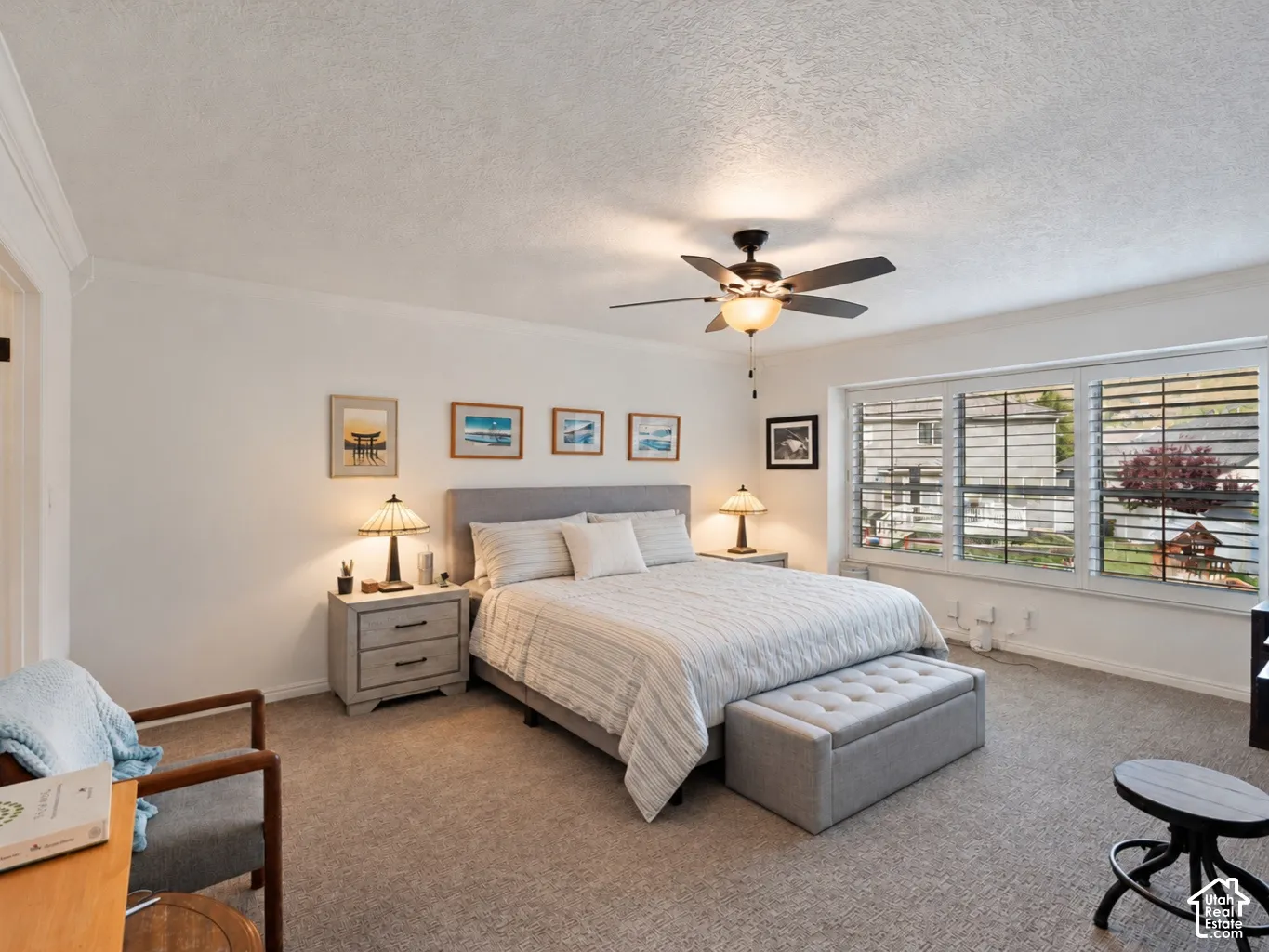 Neutral-toned interior space featuring neutral wall-to-wall carpeting, large multi-pane windows with integrated shutters, and a ceiling-mounted light fixture with a five-blade fan