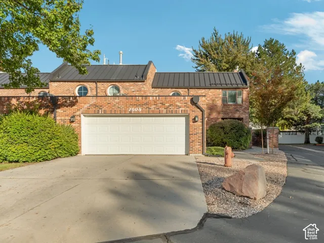 Brick exterior featuring a standing-seam metal roof, circular accent windows, and a multi-car garage with white sectional doors