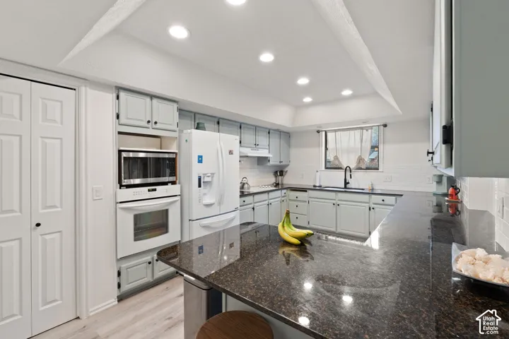 Kitchen featuring a tray ceiling with recessed lighting, stone-surface countertops, built-in dual wall ovens, light-finish cabinetry, and a matte black faucet