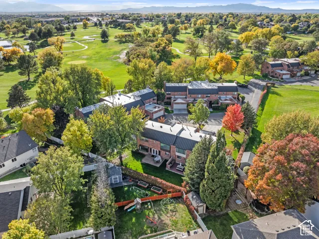 Aerial perspective of a multi-level brick exterior residence featuring a metal roof, rear paved patio, and mature landscaping