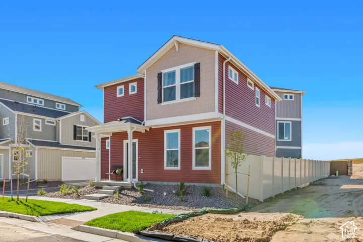 Multi-story residential exterior featuring horizontal lap and shake siding, decorative shutters, a covered front entry porch, and vinyl privacy fencing