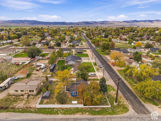 Aerial perspective of a residential property featuring a white vinyl perimeter fence, mature trees, a detached storage structure, and a mountainous horizon