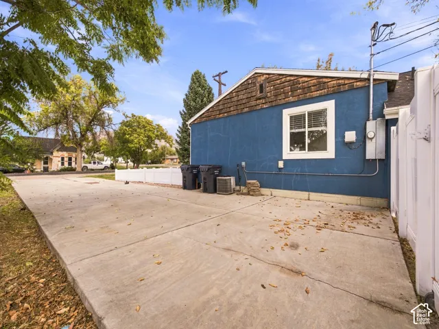 Exterior featuring blue stucco siding, wood-shake gable detailing, a white vinyl fence, and a concrete driveway