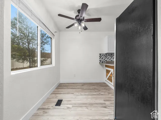 Kitchen area featuring wood-finish flooring, a large window, a ceiling fan with integrated lighting, and decorative backsplash tile
