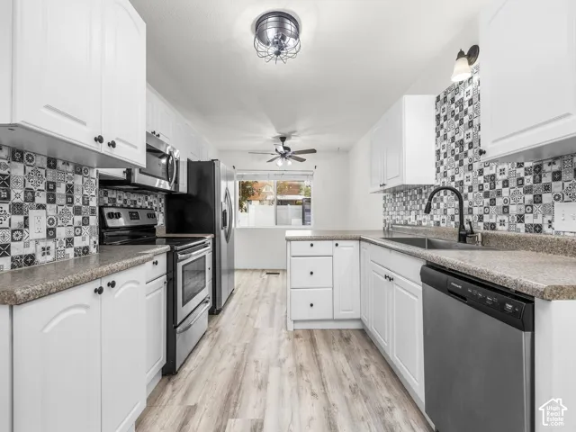 Kitchen featuring white shaker-style cabinetry, patterned tile backsplash, stainless steel appliances, and wood-finish flooring