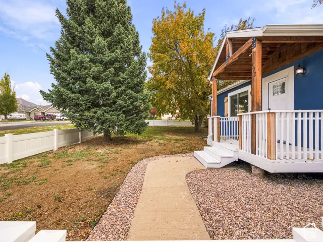 Covered wood-framed front porch with white railing, exterior concrete walkway, and white vinyl perimeter fencing