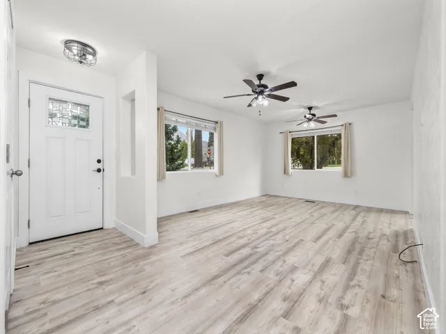 Interior space featuring wood-finish flooring, two ceiling fans with integrated lighting, dual windows, and an entry door with a decorative glass inlay