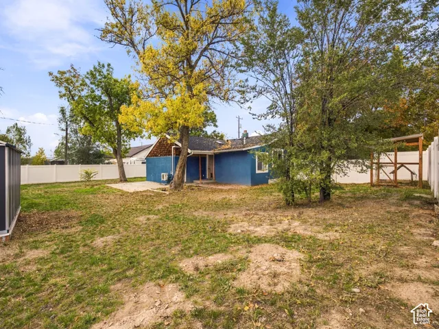 Backyard featuring a concrete patio, perimeter vinyl fencing, mature trees, and an exterior storage structure