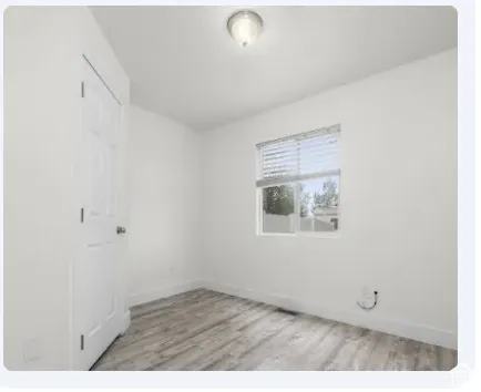 Bedroom 3, featuring wood-finish flooring, a neutral color palette, a window with horizontal blinds, and a flush-mount ceiling light