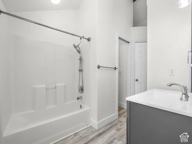 Bathroom featuring a tub-shower combination with a chrome adjustable showerhead, grey vanity with a white countertop, and wood-finish flooring