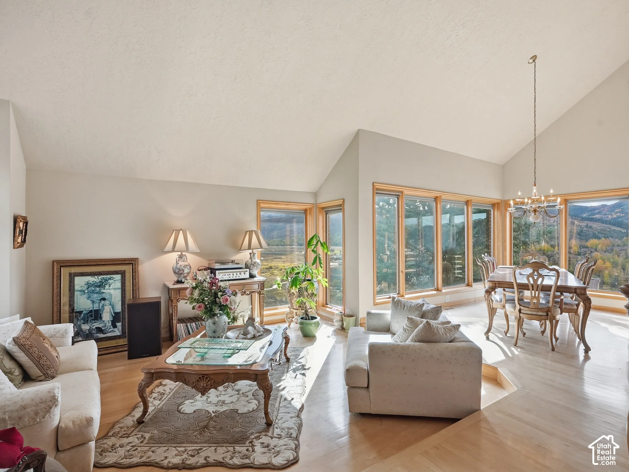 Vaulted ceilings, expansive windows with mountain scenery, wood-finish flooring, and a multi-arm chandelier