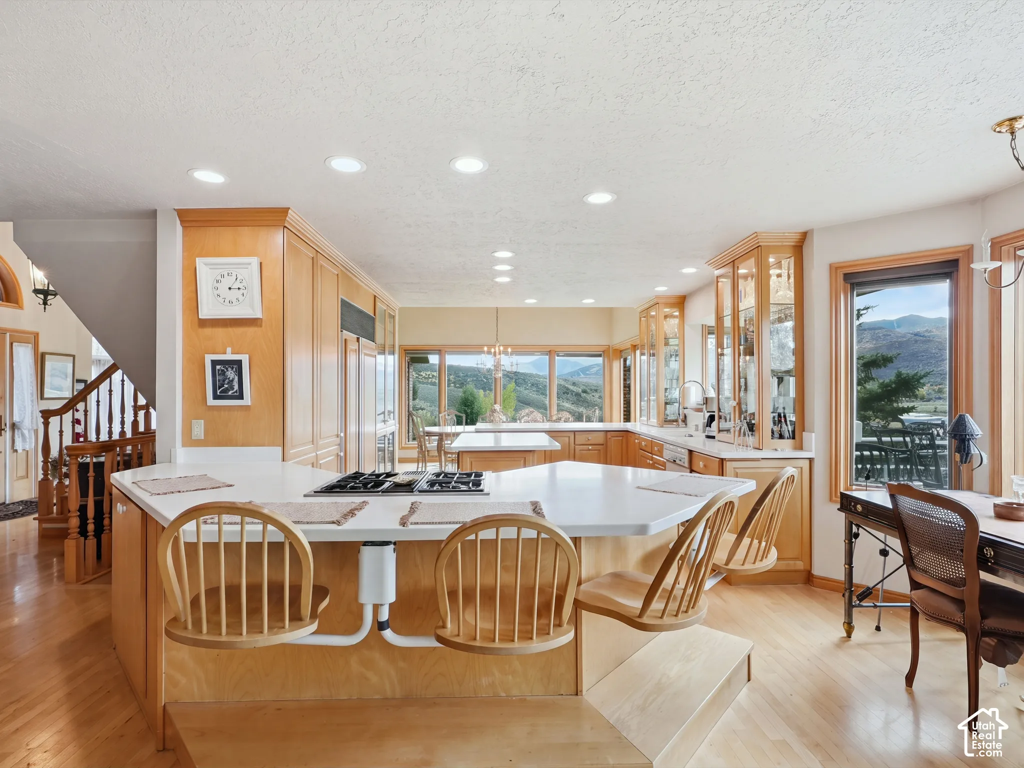 Kitchen featuring custom wood cabinetry, an expansive center island with a built-in cooktop, recessed lighting, and large windows with mountain scenery