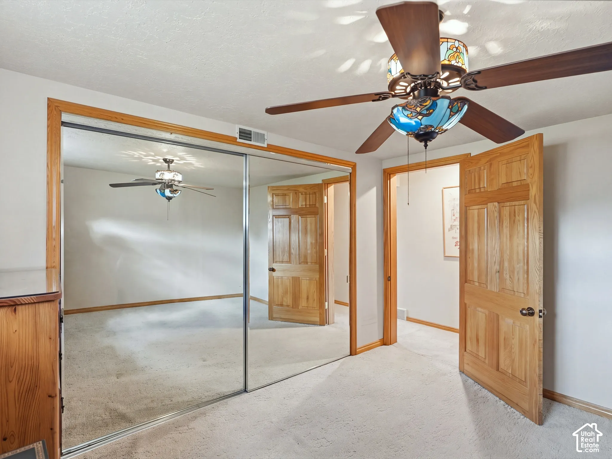 Room featuring mirrored sliding closet doors, multi-panel wood interior doors, light-toned carpet, and a stained-glass ceiling fan
