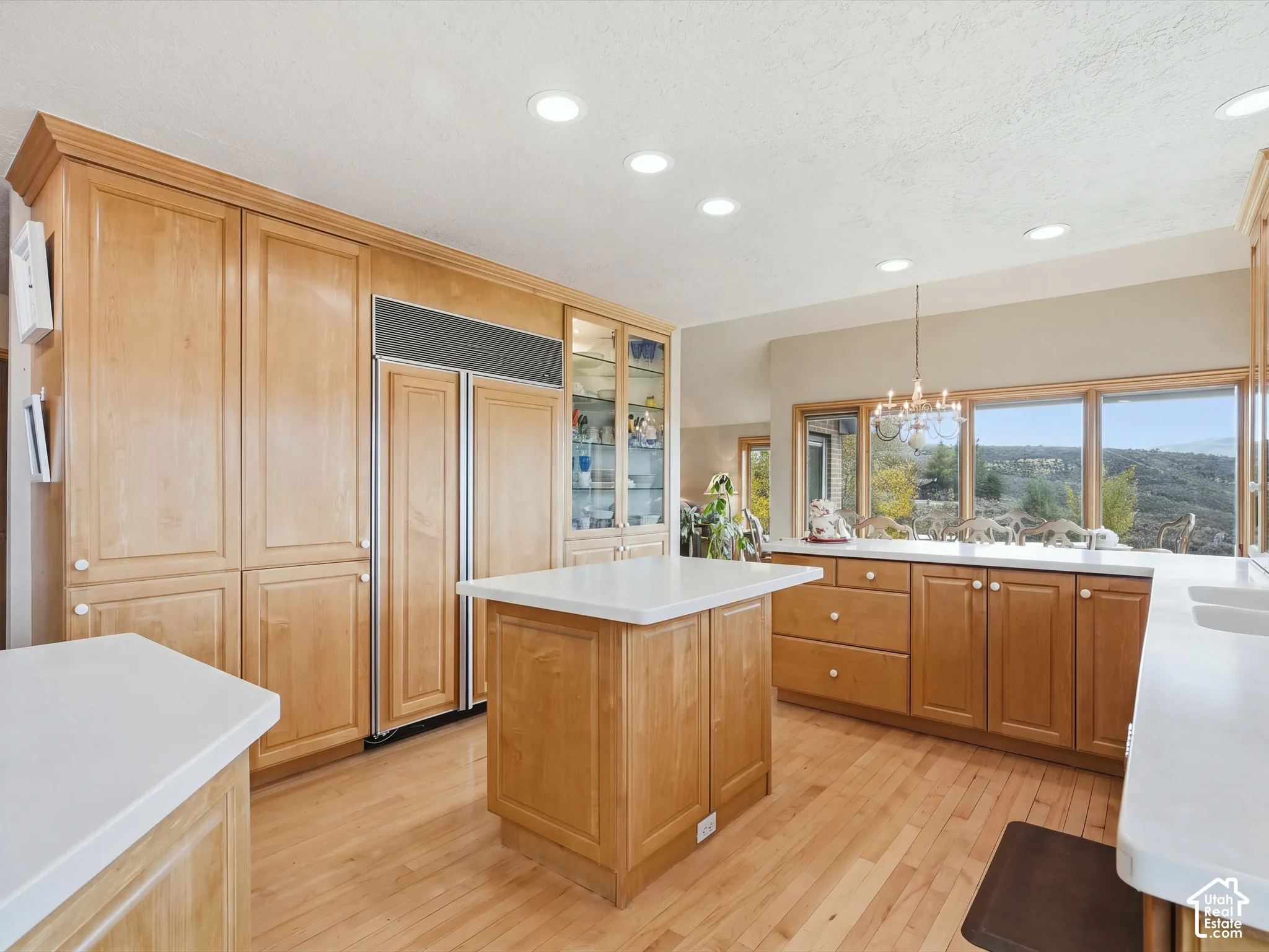 Kitchen featuring custom wood cabinetry, central island with solid-surface countertop, integrated refrigerator, recessed lighting, and wood-finish flooring