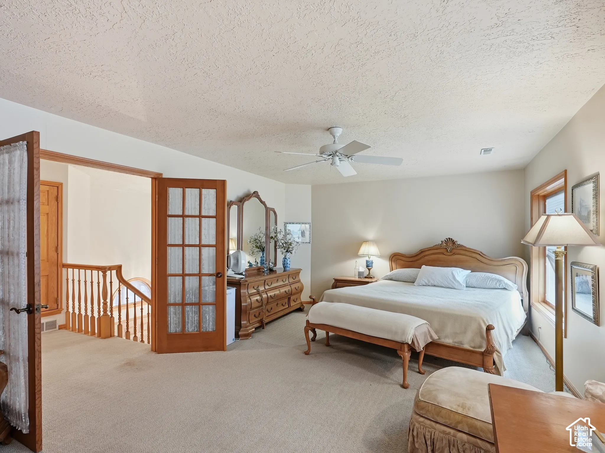 Spacious room featuring neutral carpeting, a ceiling fan with integrated lighting, wood-trimmed windows, and wood-framed French doors