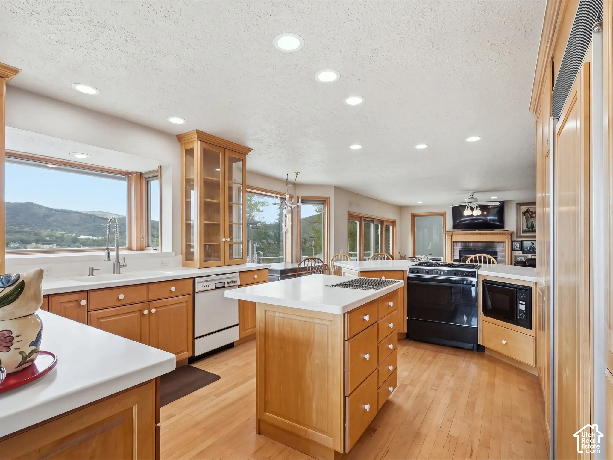 Kitchen featuring light-tone wood cabinetry, central island with integrated cooktop, white solid-surface countertops, recessed lighting, and large windows with mountain scenery