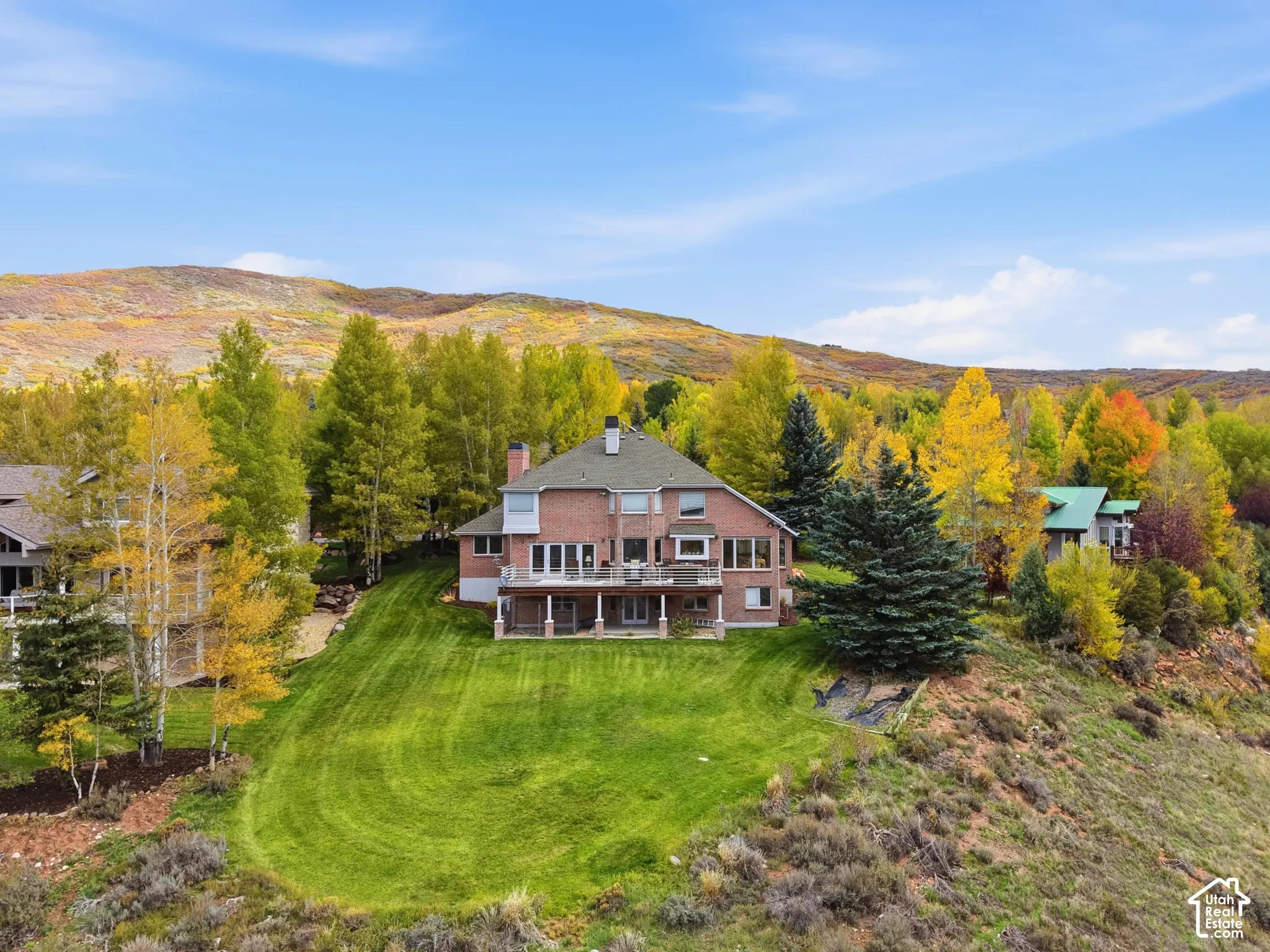 Multi-story brick residence featuring a multi-level rear deck, expansive manicured lawn, and mountain backdrop