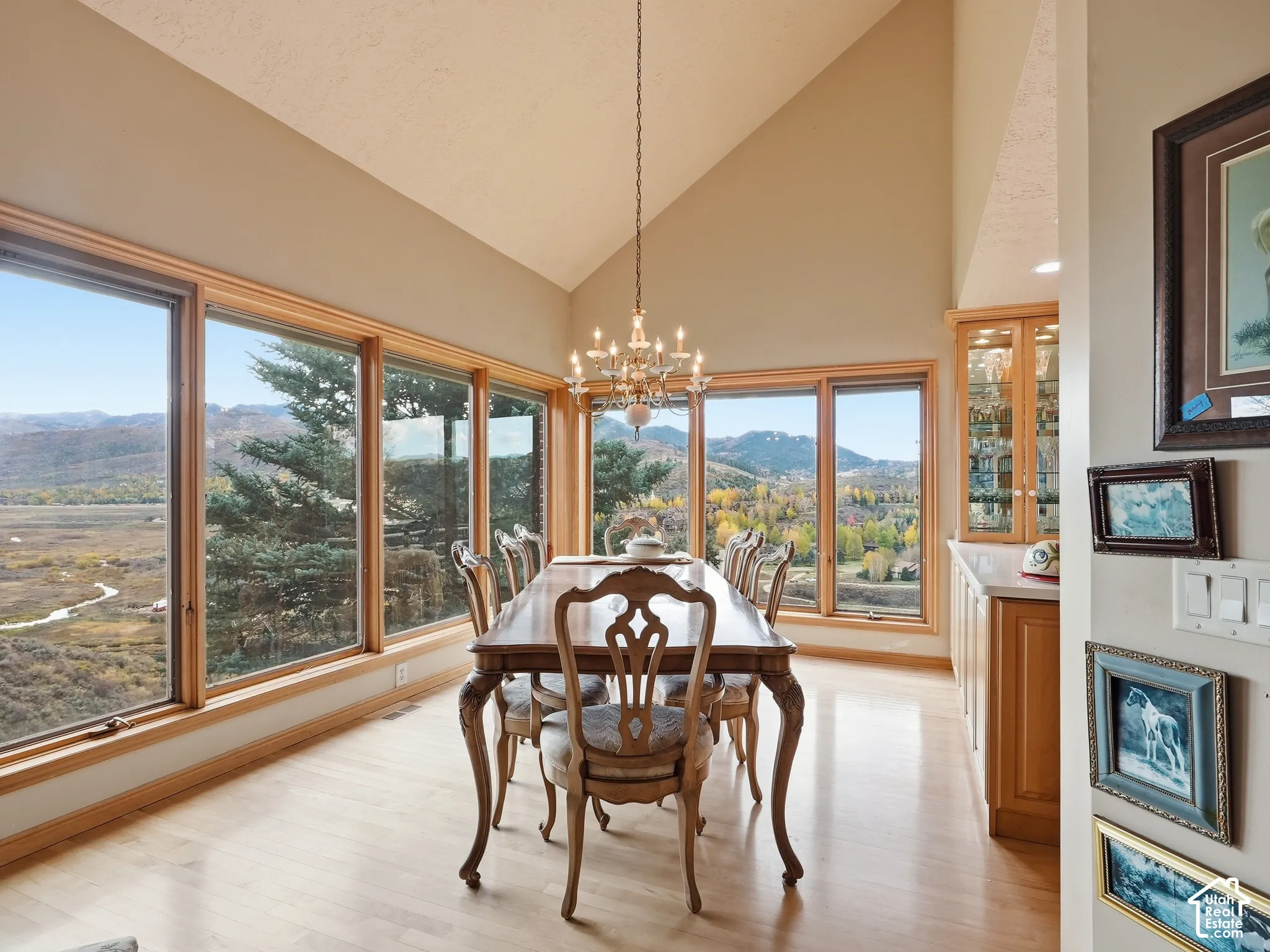 Dining area featuring a vaulted ceiling, floor-to-ceiling windows with mountain scenery, built-in cabinetry with glass-front display doors, a crystal chandelier, and wood-finish flooring