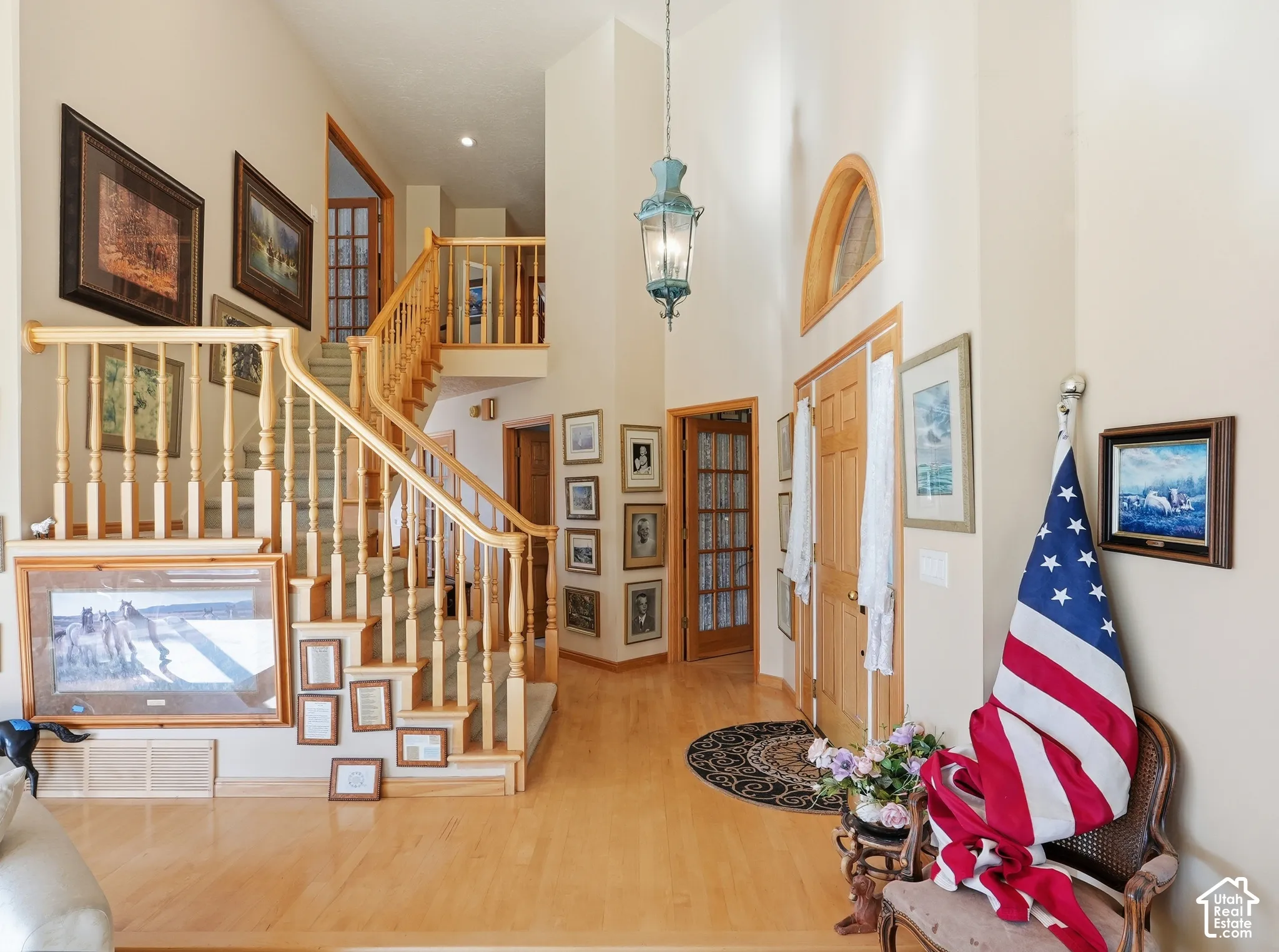 Foyer featuring double-height ceilings, wood-finish flooring, a decorative arched transom window, a prominent hanging pendant light, and a staircase with a wooden balustrade