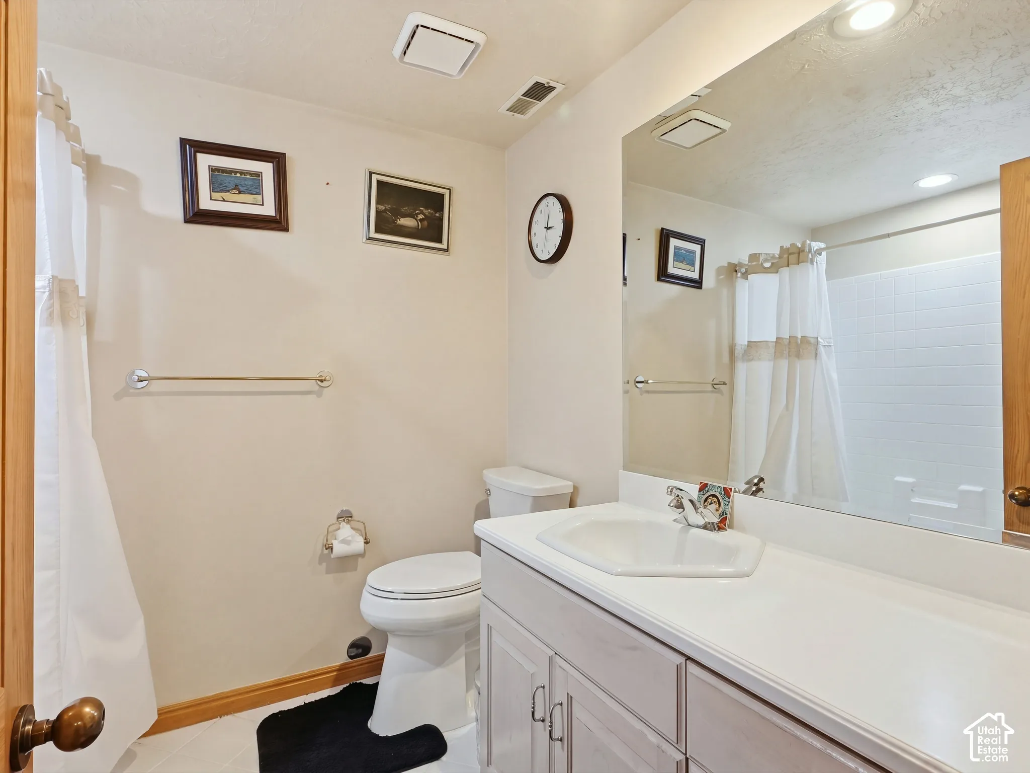 Bathroom featuring a white vanity with a molded basin, expansive wall-mounted mirror, polished chrome faucet, and a tub-shower combination with white tile surround
