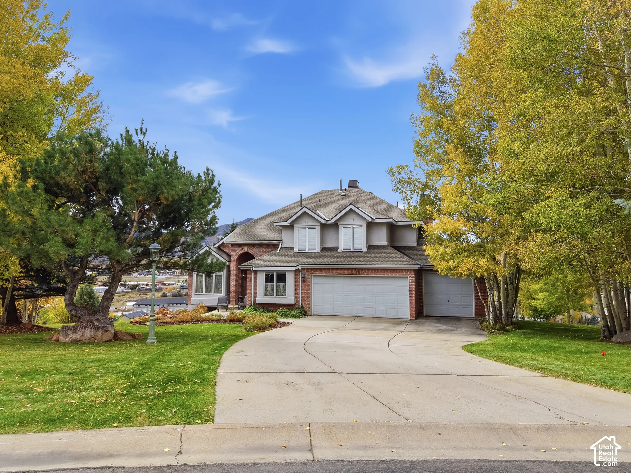 Two-story brick and siding exterior featuring a multi-gable roofline, arched entryway, and attached three-car garage, complemented by a concrete driveway and mature landscaping