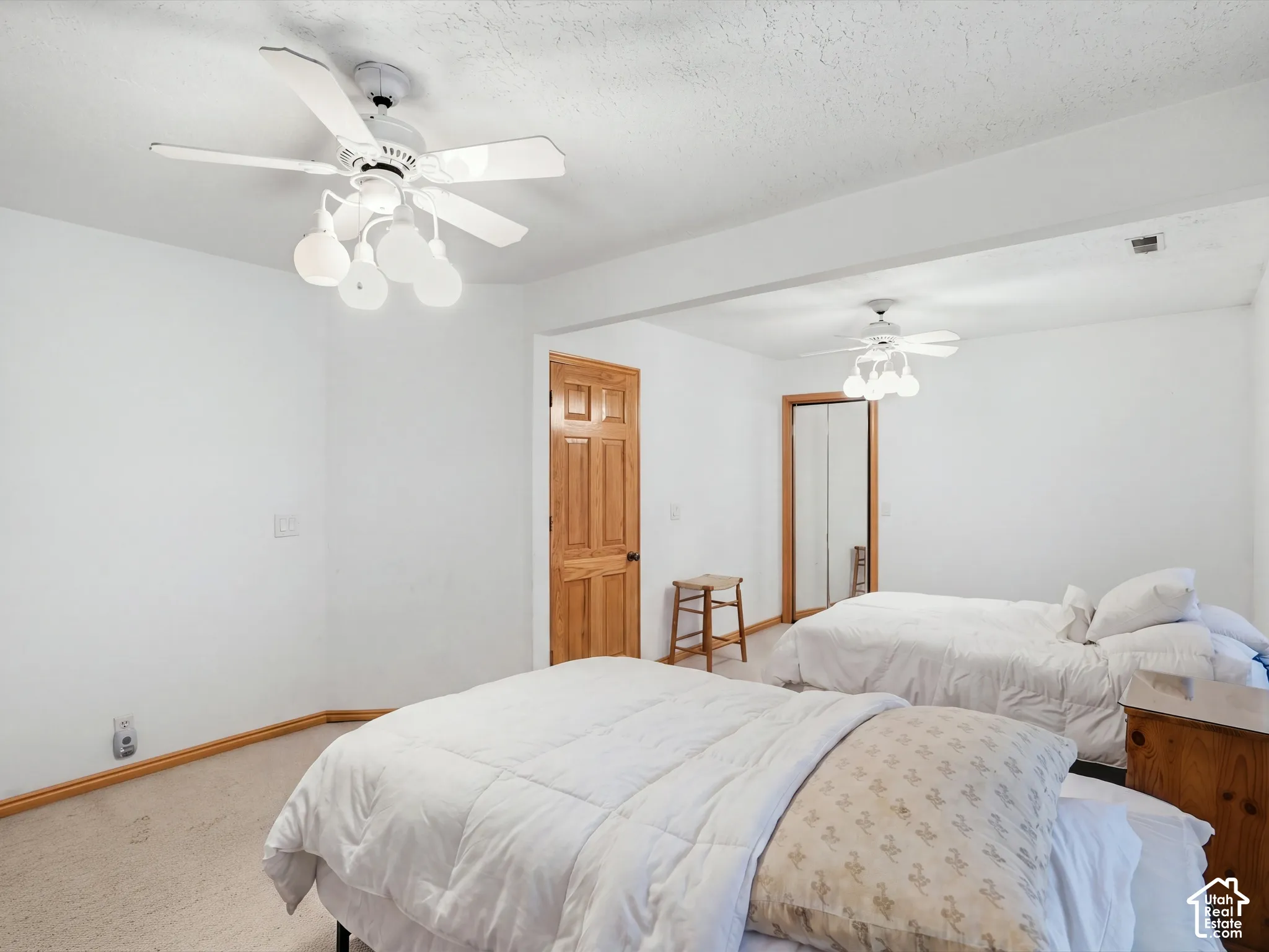 Spacious room featuring neutral carpeting, two multi-blade ceiling fans with integrated globe lighting, and a six-panel wood door