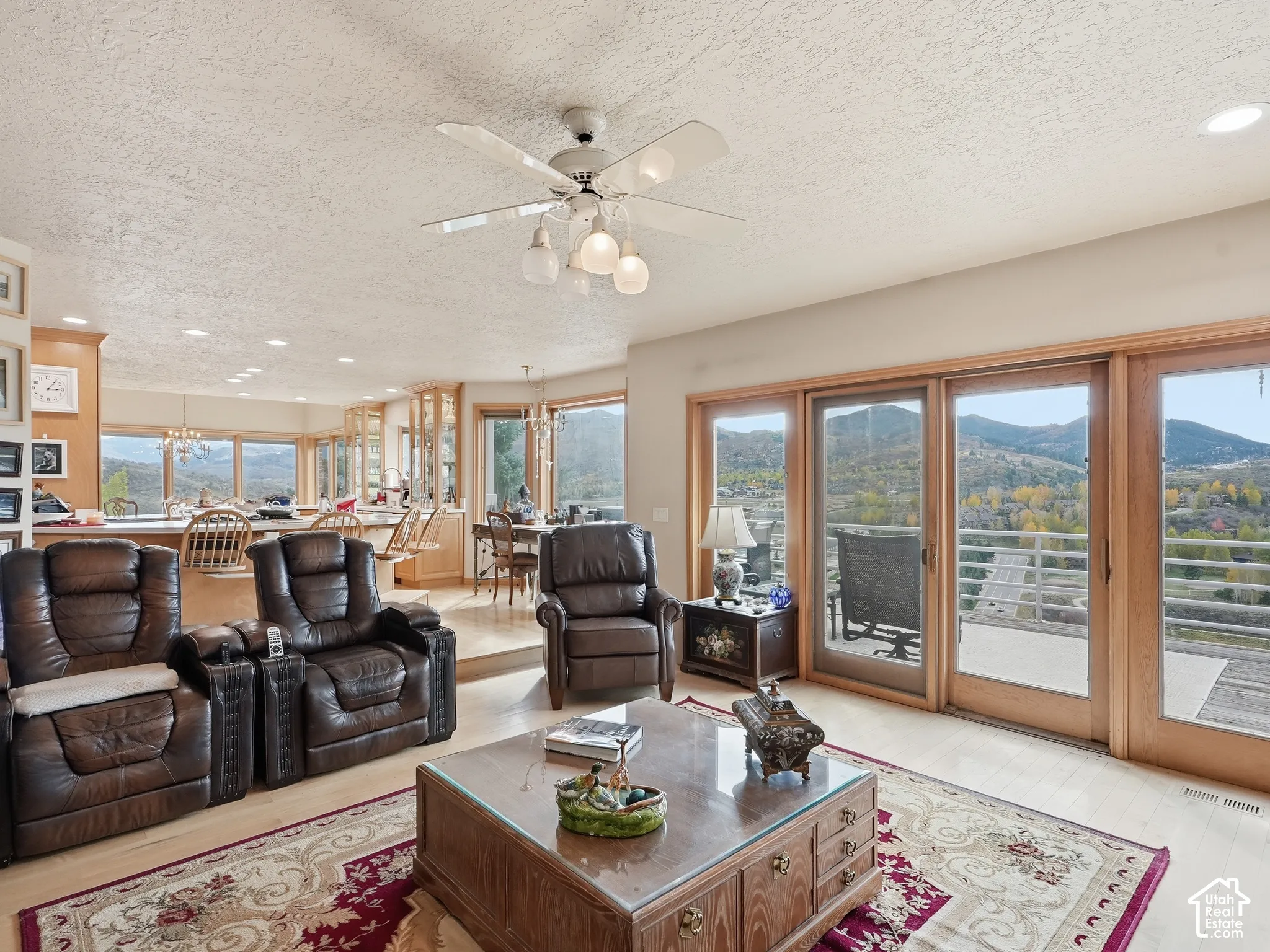 Living area featuring large wooden-framed sliding glass doors, polished light-tone flooring, ceiling fan with integrated lighting, and mountain scenery