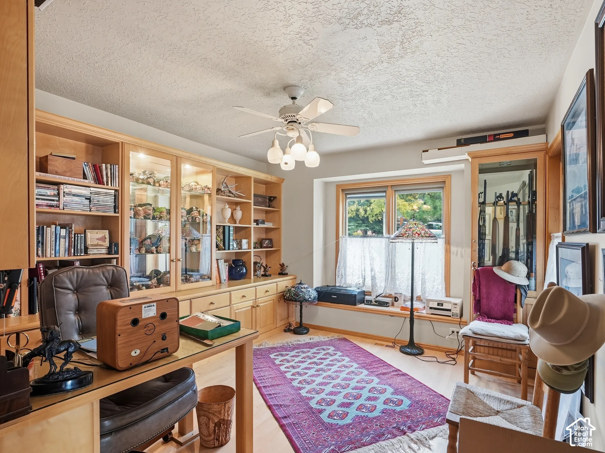 Built-in wood cabinetry with integrated glass-front display shelving, wood-finish flooring, bay window with bench seating, and ceiling-mounted fan with multi-light fixture