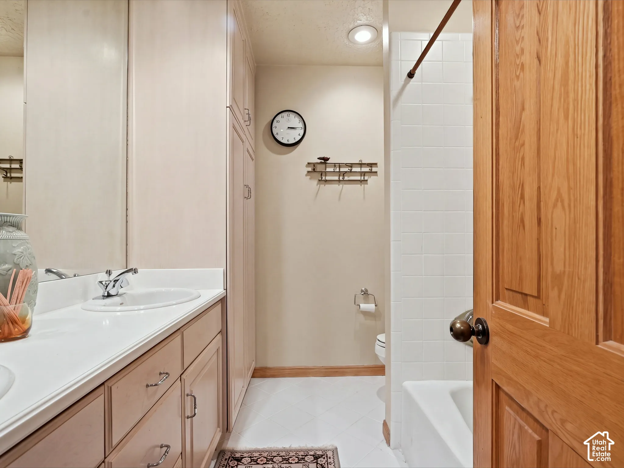Bathroom featuring a vanity with integrated sink and countertop, floor-to-ceiling built-in cabinetry, recessed lighting, and a white tiled tub surround