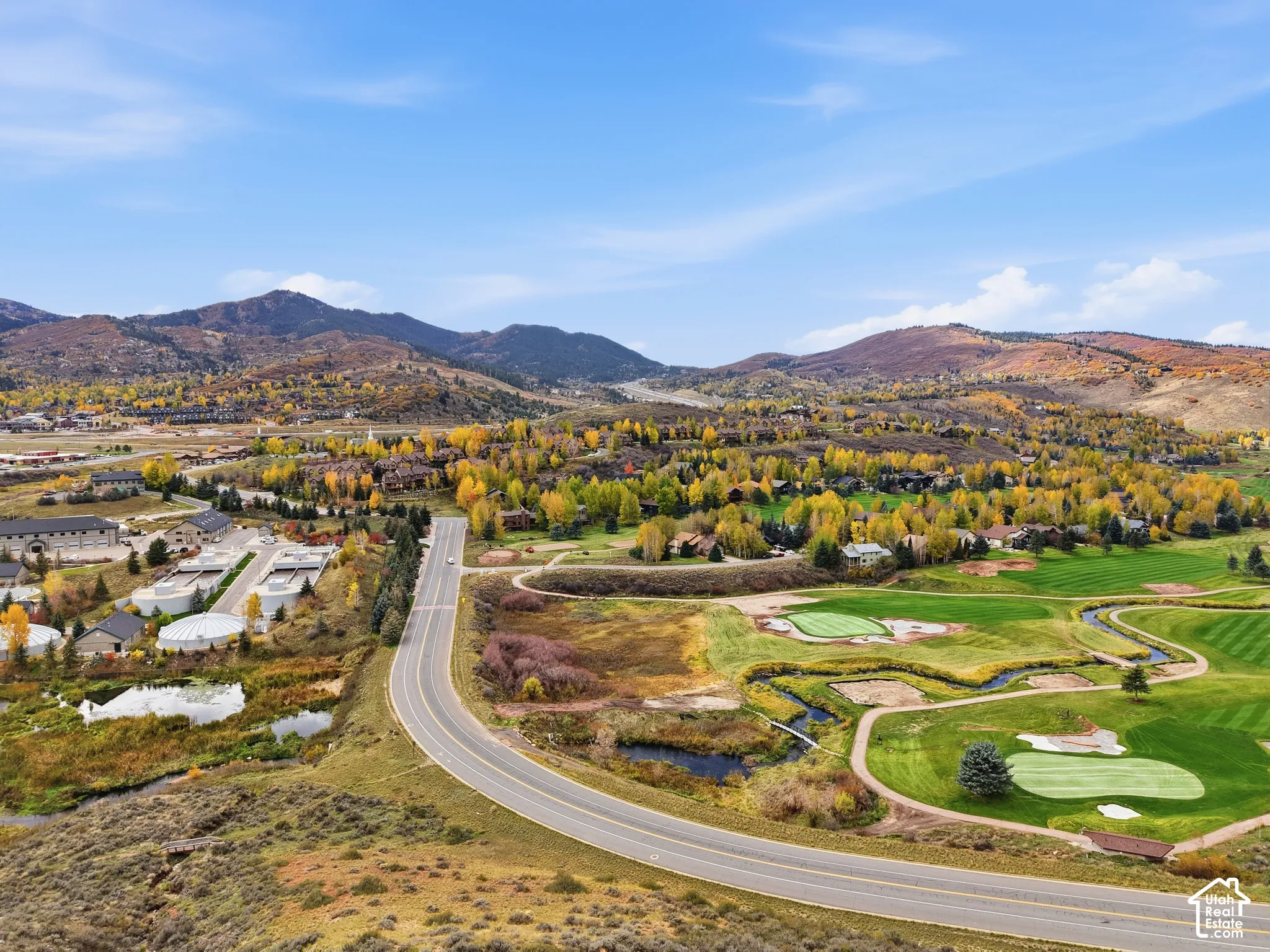 Aerial perspective featuring expansive mountain range, rolling hills, golf course fairways, natural water features, and dense mature deciduous vegetation