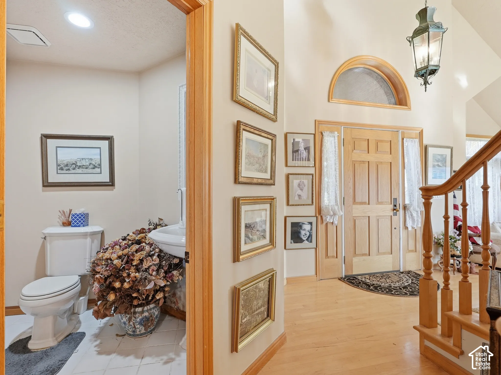Entryway featuring wood-finish flooring, staircase with wood balustrades, paneled wood door with arched transom window, and traditional pendant lighting