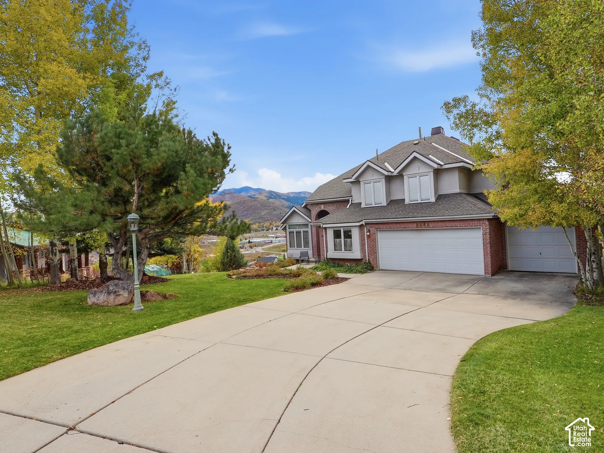 Multi-level residence featuring brick and stucco exterior, three-car garage, concrete driveway, and mountain backdrop
