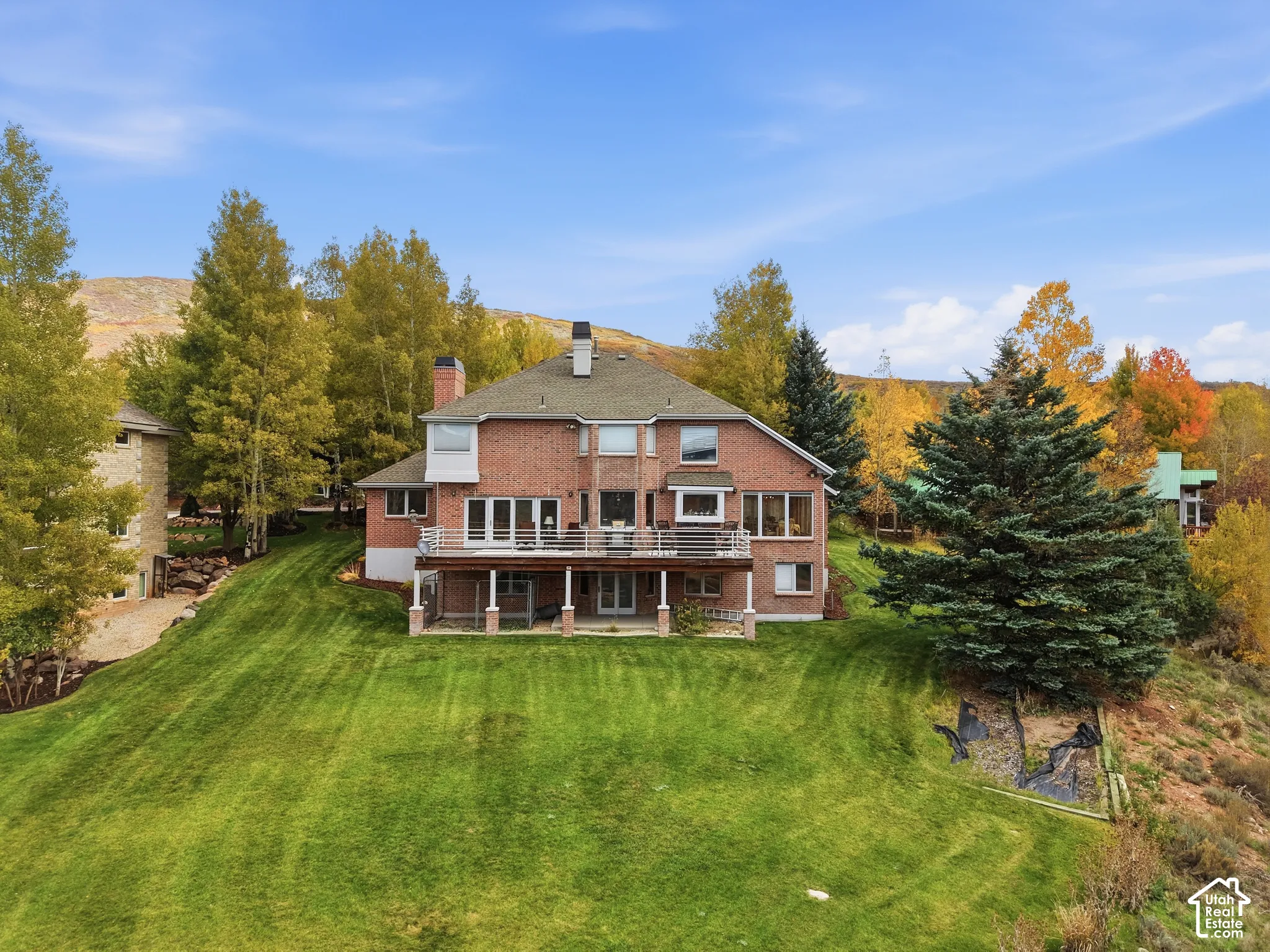 Multi-level brick exterior featuring a raised deck with metal railings, a ground-level covered patio, and large windows set against a mountainous backdrop