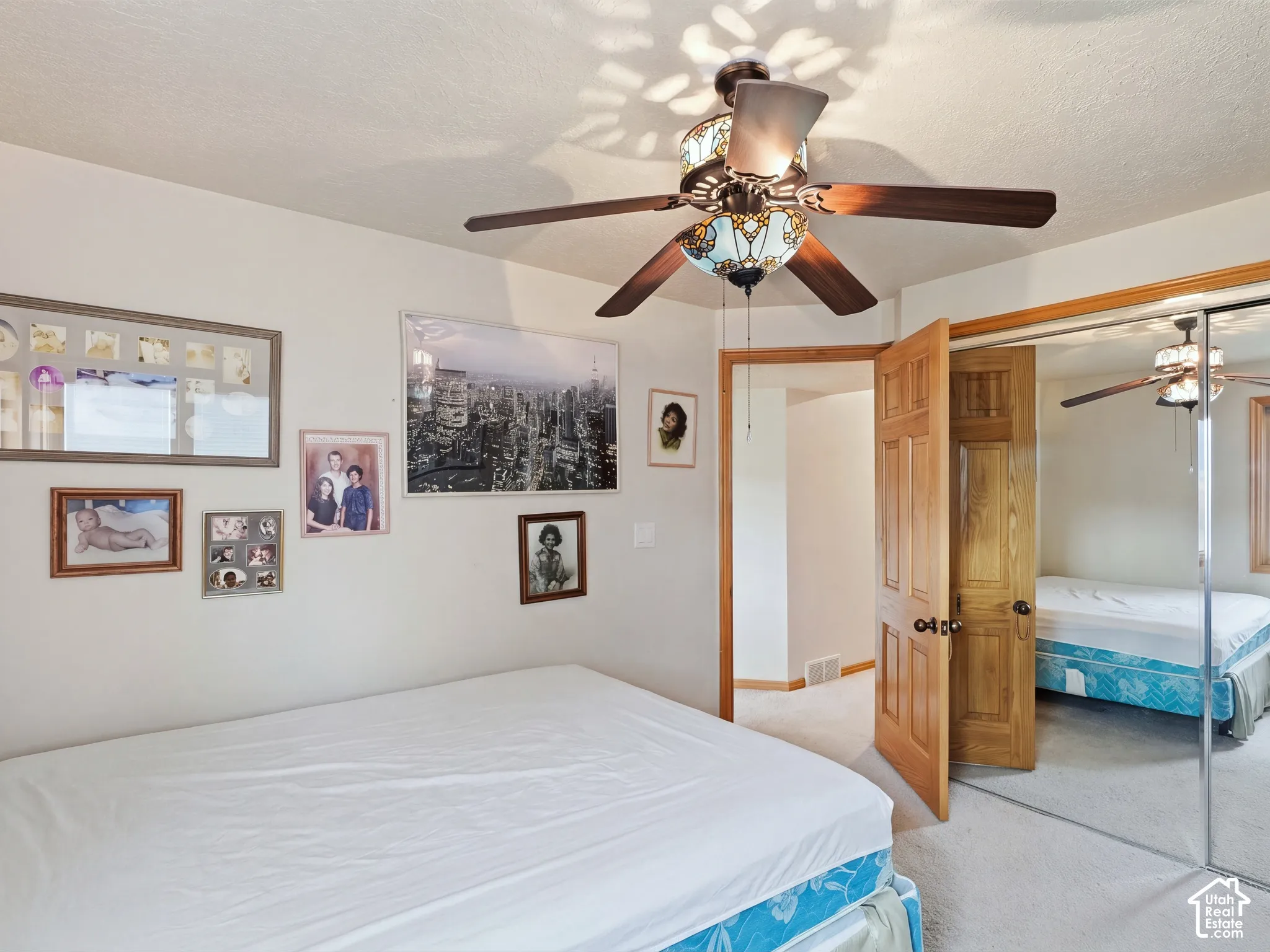 Multi-blade ceiling fan with integrated stained glass light fixture and mirrored sliding closet doors with natural wood trim
