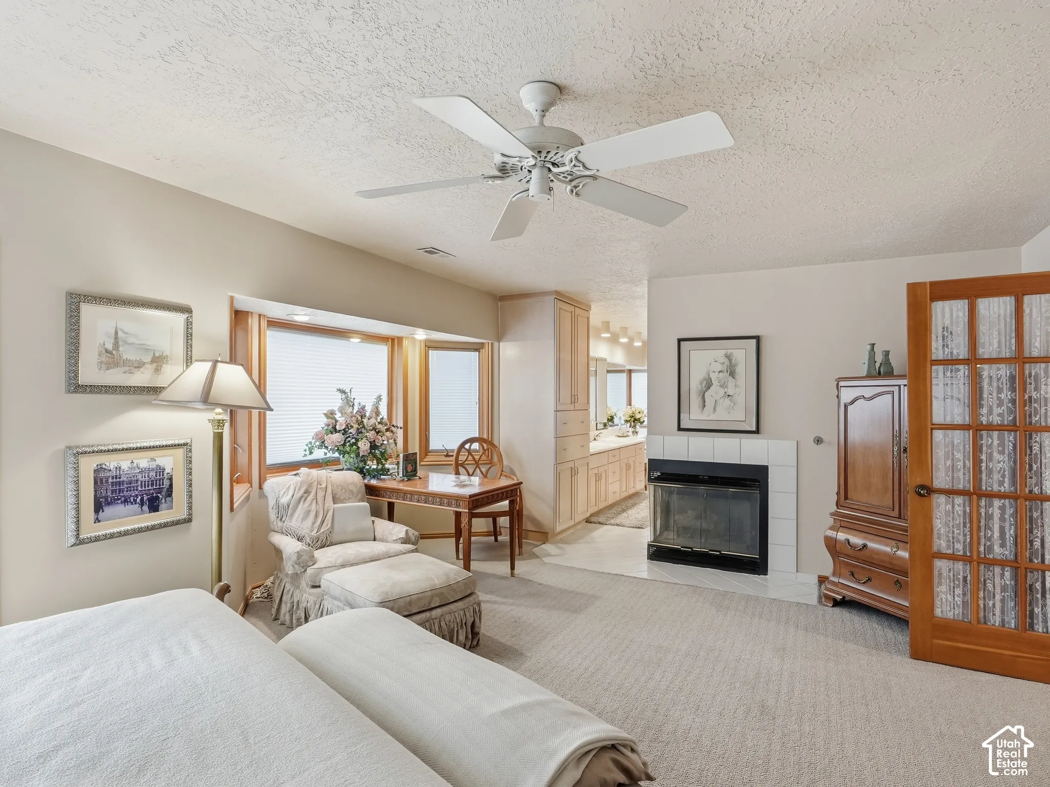 Fireplace featuring a black metal surround and tiled hearth, bay window with integrated lighting, wood-finish French doors, and ceiling-mounted fan