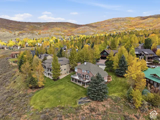Aerial perspective of a multi-level brick residence featuring an expansive elevated deck, manicured lawn, and natural mountain backdrop