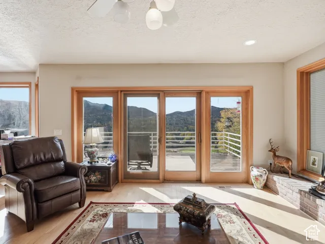 Light-filled room featuring wide-plank wood-finish flooring, floor-to-ceiling glass sliding doors with natural wood trim, a low-profile brick hearth, and expansive mountain scenery