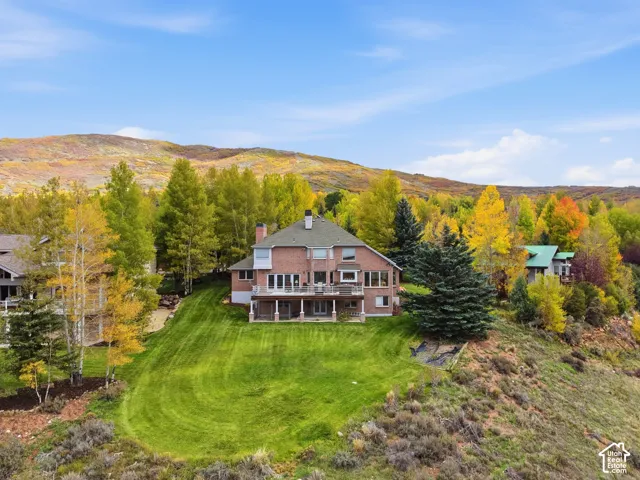 Multi-story brick residence featuring a multi-level rear deck, expansive manicured lawn, and mountain backdrop