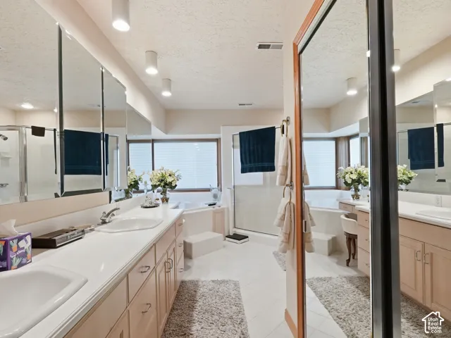 Dual-sink vanity with solid-surface countertops, expansive wall-to-wall mirrors, recessed lighting, and a built-in soaking tub