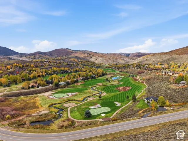 Aerial perspective featuring an expansive golf course, winding creek, natural terrain, and mountain backdrop