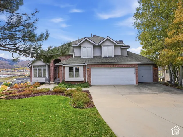 Multi-level exterior featuring brick and stucco siding, a concrete driveway, three-car garage, and dormer windows, complemented by mountain scenery