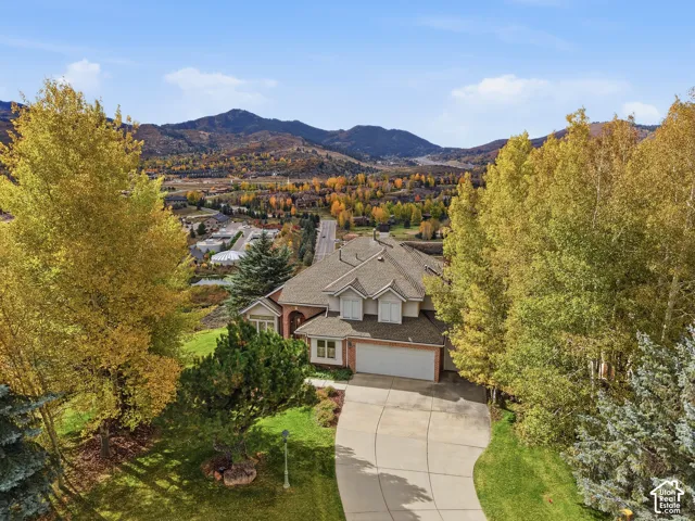 Multi-level brick and siding exterior with a shingled roof, attached multi-car garage, concrete driveway, and mature landscaping set against a mountain backdrop