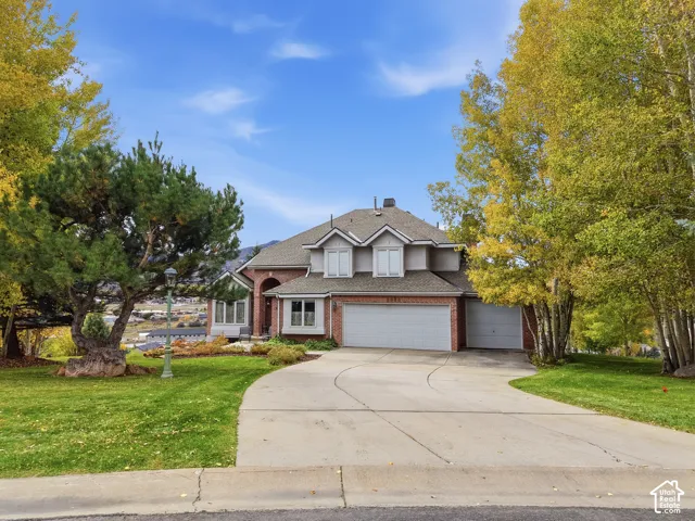Two-story brick and siding exterior featuring a multi-gable roofline, arched entryway, and attached three-car garage, complemented by a concrete driveway and mature landscaping