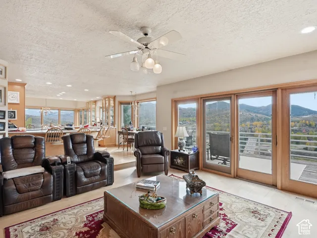 Living area featuring large wooden-framed sliding glass doors, polished light-tone flooring, ceiling fan with integrated lighting, and mountain scenery