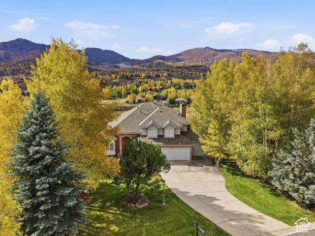 Two-story residence featuring a multi-gabled roofline, brick and siding exterior, concrete driveway, and mountain landscape backdrop