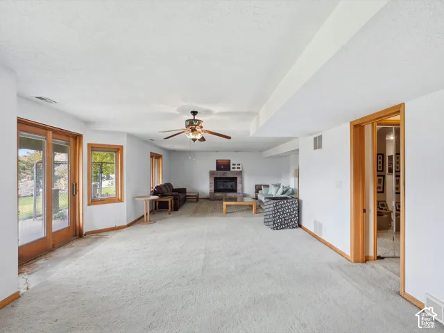 Living area featuring a floor-to-ceiling stone-faced fireplace, glass sliding doors, wood-trimmed windows, and a ceiling fan