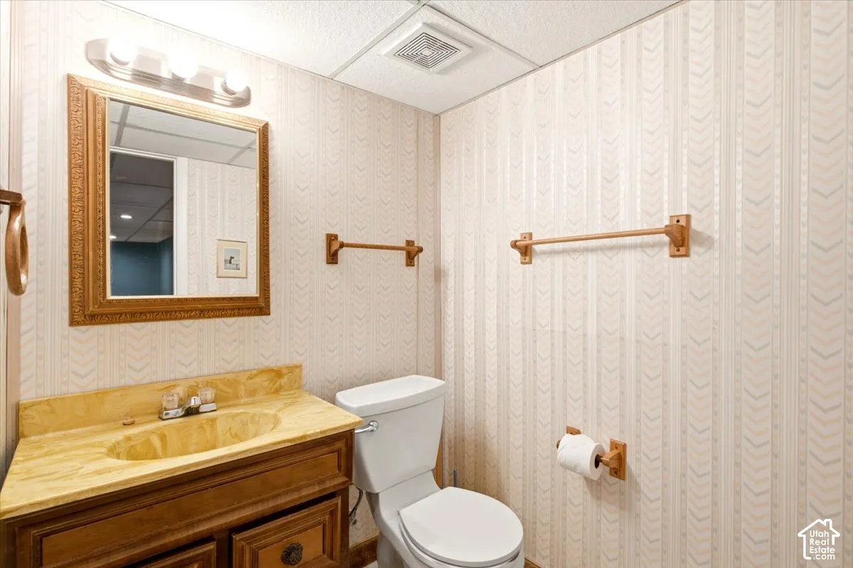 Bathroom featuring a wooden vanity, integrated basin with a stone-finish countertop, wall-mounted mirror, three-light fixture, and paper-lined walls