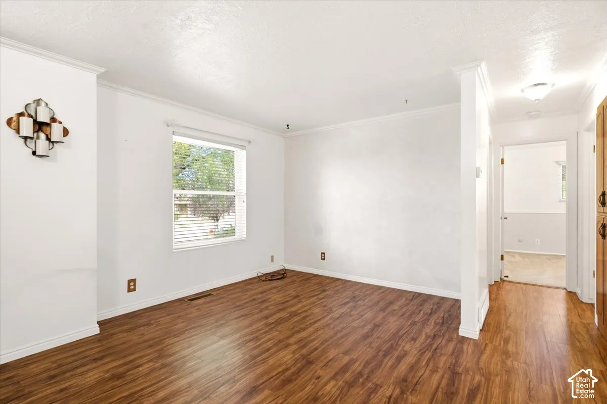 Interior space featuring wood-finish flooring, a neutral color palette, crown molding, and decorative wall-mounted lighting