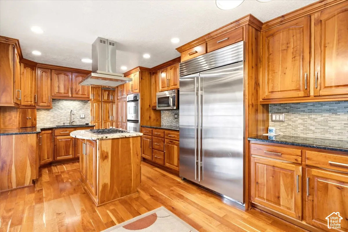 Kitchen featuring custom natural wood cabinetry, stainless steel professional-grade appliances, a central island with a gas cooktop, stone countertops, and recessed ceiling lighting